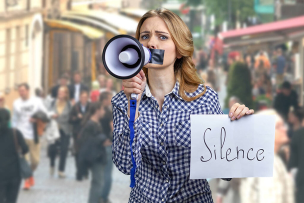 Frau mit geklebtem Mund hält Megafon und Karte mit der Aufschrift Schweigen. - Foto, Bild