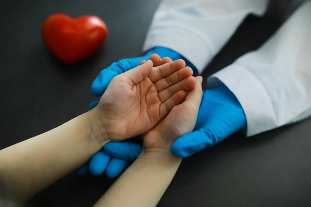 Medisch concept. De dokter in handschoenen houdt de hand van de patiënt vast. De morele hulp van de dokter aan zijn patiënten. Cardioloog consultatie. Epidemisch. - Foto, afbeelding