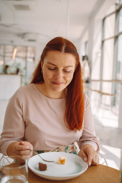 Portrét kavkazské romantické blogger žena jí sladký dezert a těší sedí u stolu v kavárně - Fotografie, Obrázek