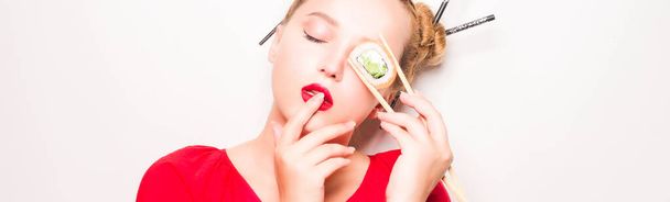 Woman in red kimono eats philadelphia sushi with chopsticks, enjoys. Red lipstick and Japanese hairstyle, space for text. Beautiful girl fashion photo on a white background. - Foto, immagini