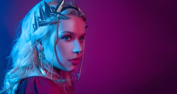 Queen in a silver crown in neon in blue and red. Theme party, place for text. Blonde mother of dragons. Evening make-up, jewelry. - Fotografie, Obrázek
