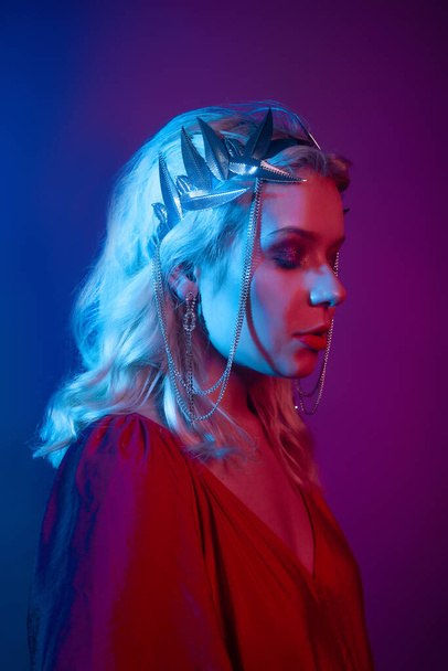 Queen in a silver crown, trendy stylish neon photo. The woman is all in jewelry and bijouterie. Red blue light. Evening make-up, red lips and shadows in sparkles. - 写真・画像