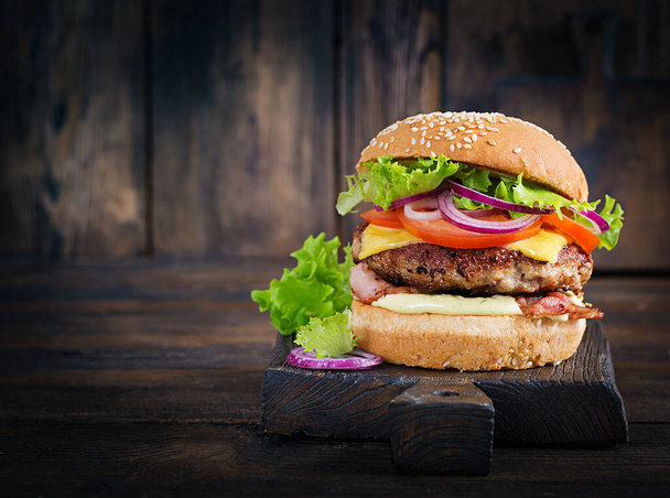 Hamburger z bekonem, mięso z indyka, ser, pomidor i sałata na drewnianym tle. Smaczny hamburger. Zamknij się. - Zdjęcie, obraz