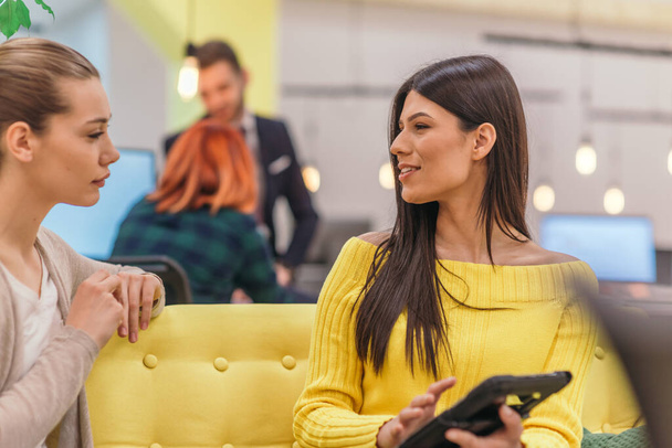 Multiethnic kolegové blond běloška a Latina tmavovlasá Handsome businesswomen (zaměstnanec) sedí na žlutém gauči při práci na notebooku v moderní startup společnosti - Fotografie, Obrázek