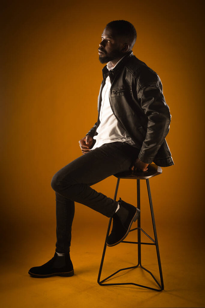 Красивий чорний хлопець сидить на високому стільці, позуючи на жовтому тлі
 - Фото, зображення