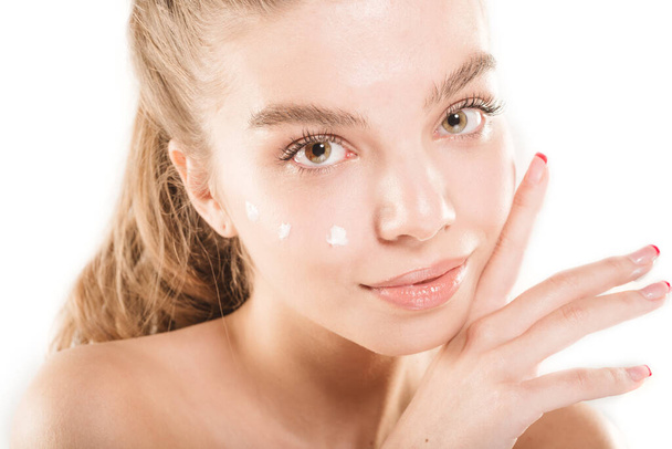 Primer plano retrato de una hermosa joven con piel fresca y crema en su cara mientras posa en el estudio - Foto, Imagen
