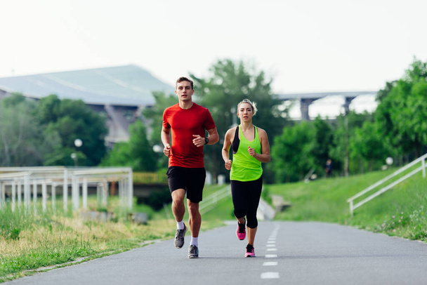Giovane coppia che corre facendo jogging su una strada asfaltata nel parco - Foto, immagini