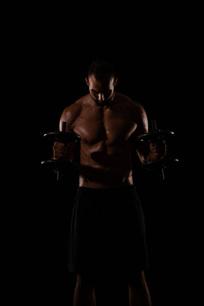 Topless i przystojny facet ćwiczy z ciężarkami, koncentrując się na swoich mięśniach - Zdjęcie, obraz