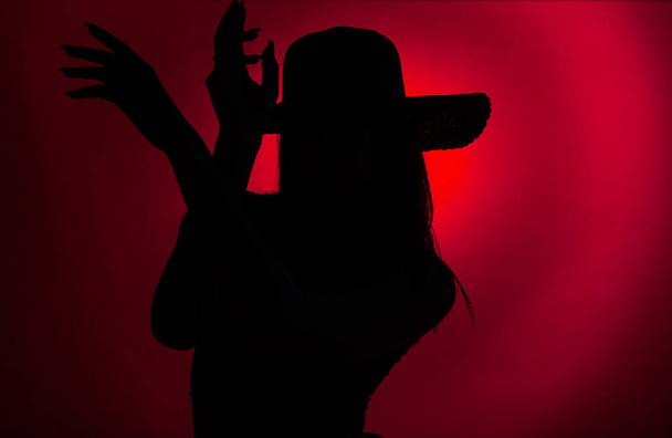 Καταπληκτική και σκούρα κόκκινη σιλουέτα ενός νεαρού κοριτσιού που ποζάρει με τα χέρια στο στούντιο ενώ κοιτάζει σαγηνευτικά - Φωτογραφία, εικόνα