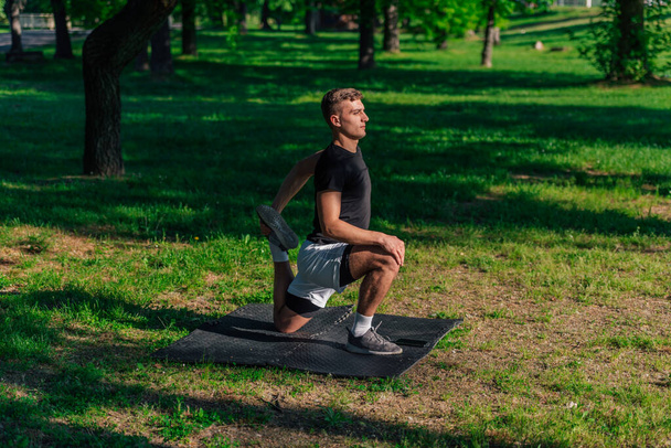 Αθλητικός νεαρός άνδρας τεντώνει τα πόδια και κάνει εμπρός lunge ενώ έχουν προπόνηση στο πάρκο - Φωτογραφία, εικόνα