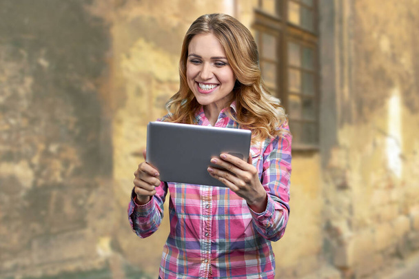 Mladá usměvavá žena při pohledu na tablet PC na pozadí staré budovy venku. - Fotografie, Obrázek