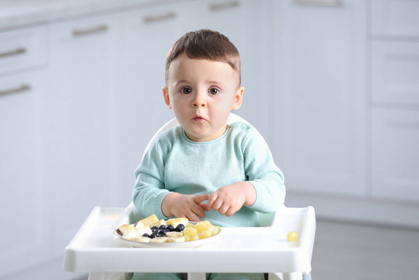 Cute little baby eating healthy food in high chair at home - Foto, immagini