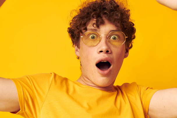 Young curly-haired man yellow t-shirt glasses fashion hand gestures isolated background unaltered - 写真・画像