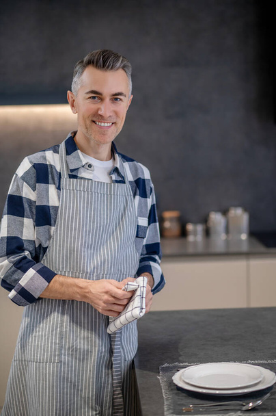 Happy man in apron with napkin looking at camera - 写真・画像