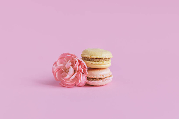 Lekkere franse macarons met bloemen op een roze pastelachtergrond. Plaats voor tekst. - Foto, afbeelding