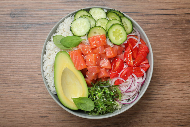Delicious poke bowl with salmon and vegetables on wooden table, top view - Fotó, kép