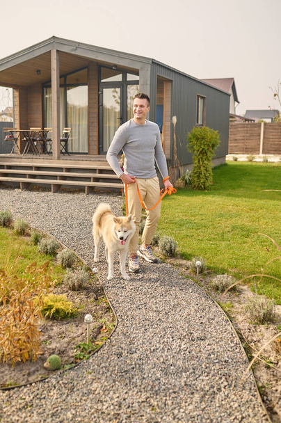 Man with dog on leash walking near country house - Zdjęcie, obraz