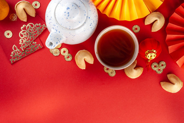 中国の旧正月の背景。伝統的な中国の新年の装飾が施された赤と金色の黄色のフラットレイ、願いを込めた封筒、金貨、ファン、中国の提灯、オレンジと紅茶 - 写真・画像