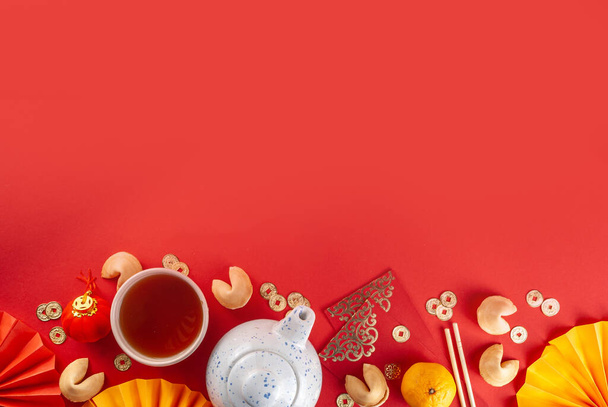 Chinese nieuwjaarsachtergrond. Rood en goudgeel plat met traditioneel Chinees nieuwjaarsdecor, enveloppen met wensen, gouden munten, waaiers, Chinese lantaarns, sinaasappels en thee - Foto, afbeelding
