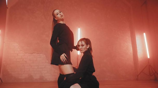 Two beautiful girls dancing in a room with red lighting in black and white suits. Dances - Photo, Image