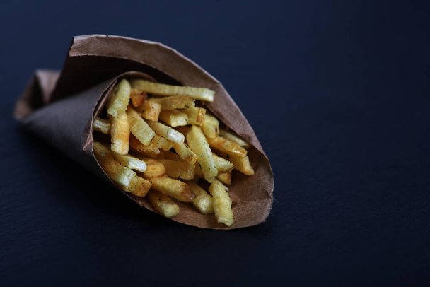 fast food concept - paper cone of french fries isolated on dark background. Image contains copy space - Foto, Imagem