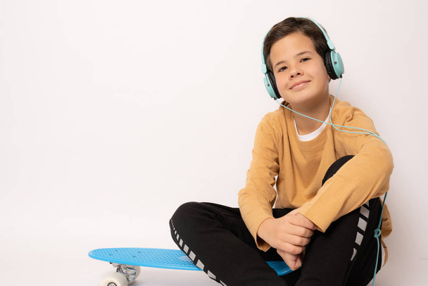 Bonito menino usando fones de ouvido com skate isolado sobre fundo branco. - Foto, Imagem