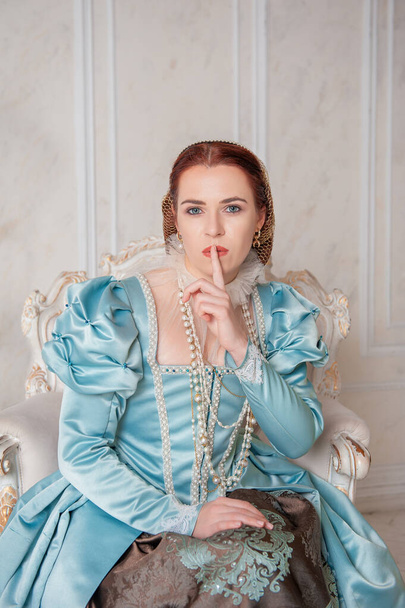Beautiful young woman in medieval style blue dress with finger on lips - Photo, Image