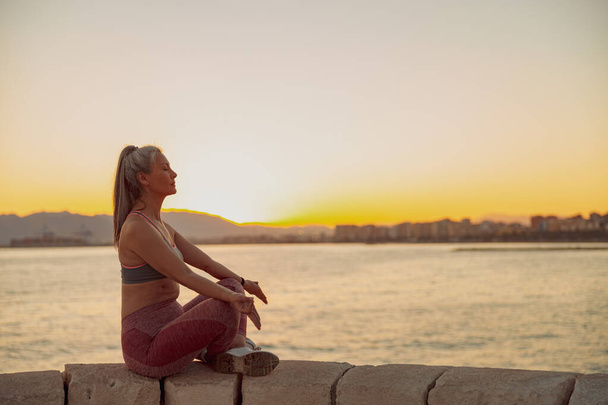 Sportiva asiatica pratica yoga, seduta sul bordo in riva al mare - Foto, immagini