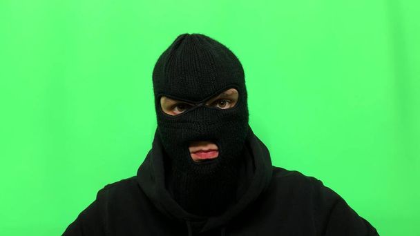 Angry young man has become a thief and prepares his equipment and clothes on a green background in a balaclava for the first store robbery - Foto, imagen