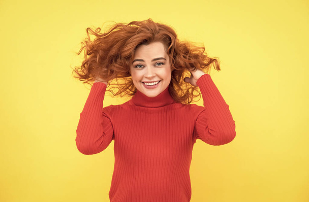 heureuse rousse femme avec des cheveux bouclés venteux sur fond jaune, soins des cheveux - Photo, image