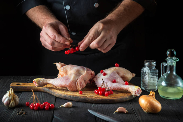 Le chef prépare des cuisses de poulet crues dans la cuisine du restaurant. Le cuisinier met le viorne rouge sur la cuisse de poulet avant la cuisson. Plat national. - Photo, image