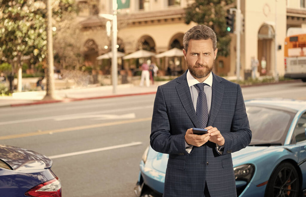 successful man in suit stand by car texting on smartphone, copy space, rent online. - Fotó, kép