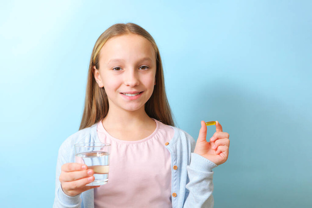 A teenage girl holds an omega 3 capsule in her hands on a colored background.  - Photo, Image