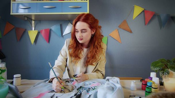 The general plan of a beautiful red-haired girl drawing with multicolored paints on clothes. Handmade work - Foto, afbeelding