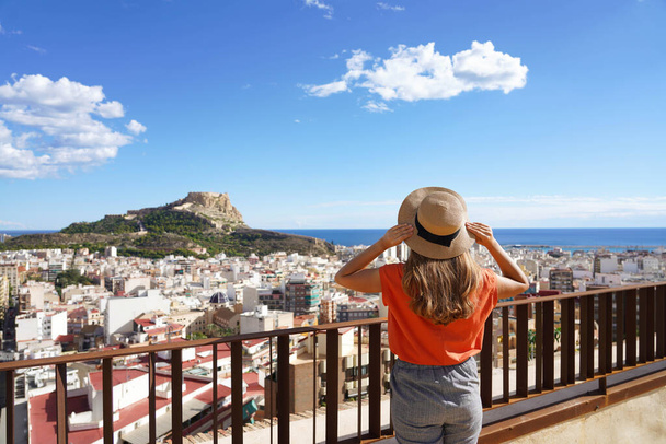 Női turista gazdaság kalap és nézi Alicante városkép és Mount Benacantil a Santa Barbara Castle és a tenger a háttérben, Spanyolország - Fotó, kép