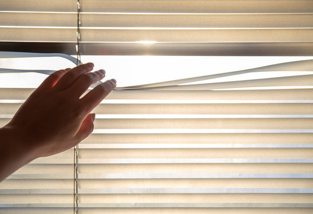 Womans hand taking a peak through the window blinds. - Foto, Bild