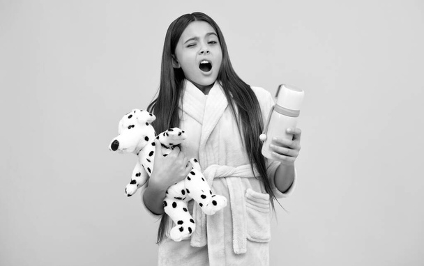 sbadigliare giovanissima ragazza in casa spugna accappatoio con giocattolo e thermos bottiglia, sbadigliare - Foto, immagini