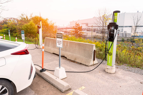 Estación de carga para coches eléctricos en un estacionamiento con una central nuclear en segundo plano. Ontario, Canadá. - Foto, imagen