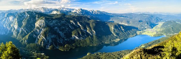 Panoramic photo of high rocky mountains of Julian Alps in Slovenia with blue lake Bohinj in the valley. - Photo, Image