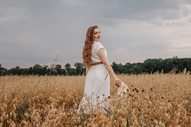 Tyttö valkoisessa mekossa kävelee kaurapellolla. Kuva iloinen tyttö valkoinen mekko nauttia elämästä vehnä niitty kesällä. Kaura. Kaunis onnellinen nainen hauskaa vehnäpellolla. - Valokuva, kuva