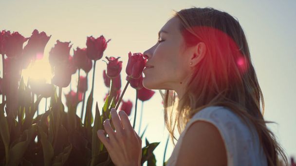 Nahaufnahme weibliche Blütenknospe berühren. Lächelndes Mädchen genießt Tulpe in Sonnenstrahlen. - Foto, Bild