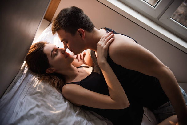 Close-up portrait of a couple in love lying on a bed at home, tenderly hugging each other and kissing. Newlyweds morning. The lovers watch spend the weekend together. The concept of tactility - Foto, Bild
