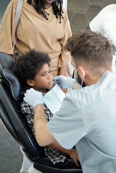 Young dentist putting napkin on chest of little patient - Photo, Image