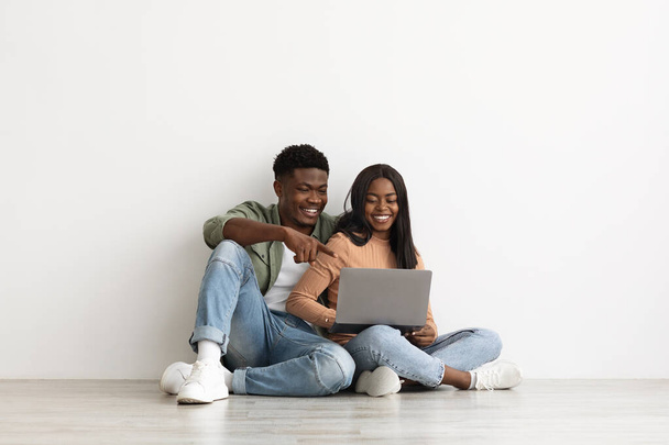 Happy black couple sitting on floor with laptop, having conversation - Φωτογραφία, εικόνα
