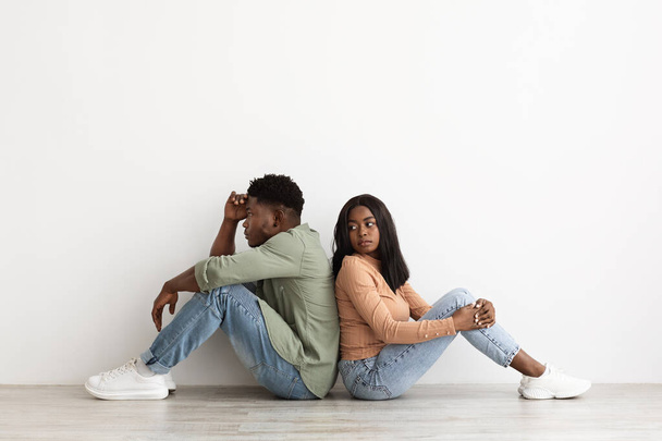 Frustrated african american couple sitting back to back on floor - Fotó, kép