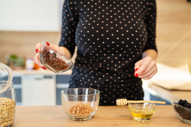 Nahaufnahme der Hände einer unbekannten kaukasischen Frau, die zu Hause gesundes Frühstück mit Haferflocken und Trockenfrüchten zubereitet - Foto, Bild