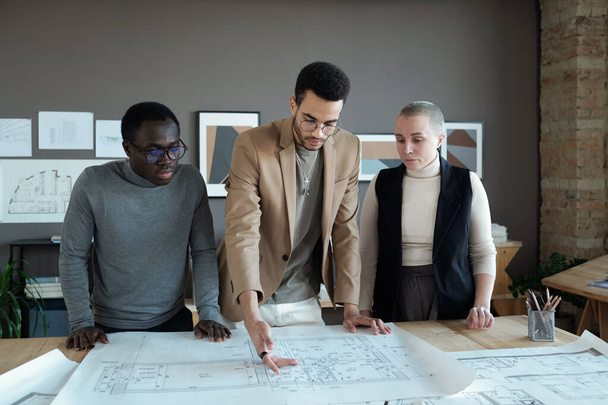 Young biracial businessman making presentation of sketch on unrolled blueprint - Photo, Image