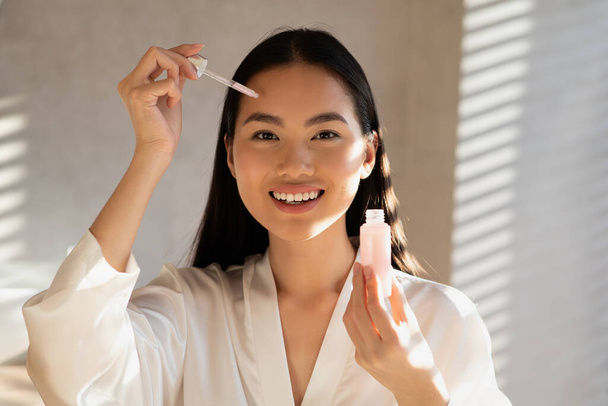 Cheerful pretty chinese woman applying beauty product on forehead - Fotó, kép