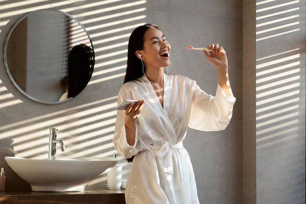幸せな韓国人女性歌ながらブラッシング歯でバスルーム - 写真・画像
