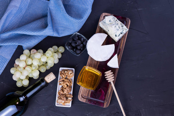 vista superior de un aperitivo surtido de queso azul dor y camembert en una tabla de madera con miel y uvas y con una botella de vino - Foto, Imagen